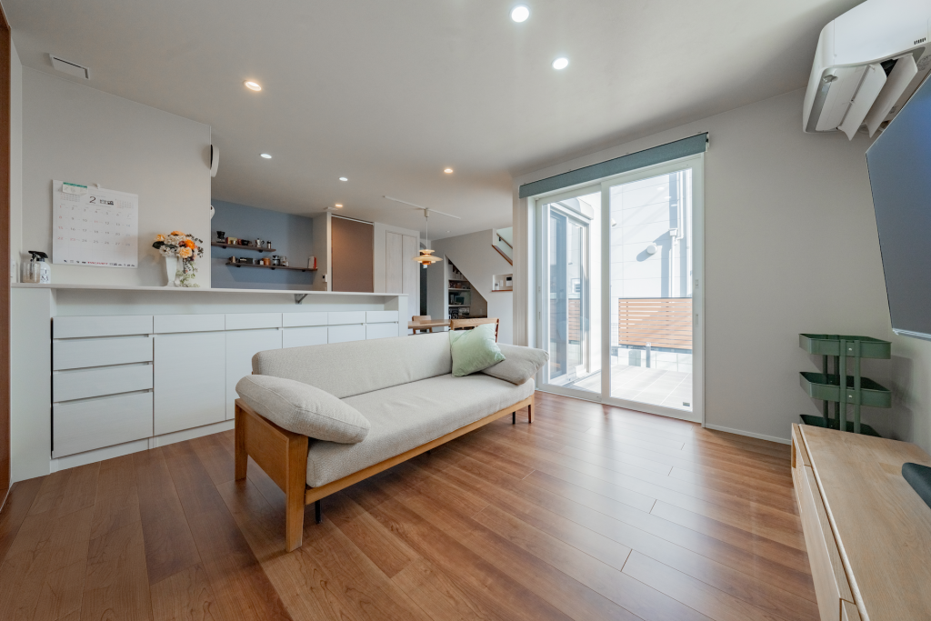 大開口サッシからバルコニーへつながる明るいLDK。対面キッチンと白い収納カウンターのあるナチュラル空間