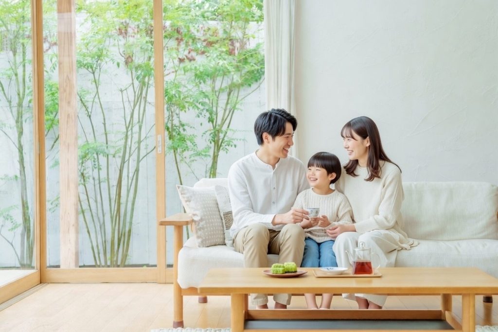 大きな窓から緑が見える明るいリビングで、ソファに座る家族3人が笑顔で団らんしている様子