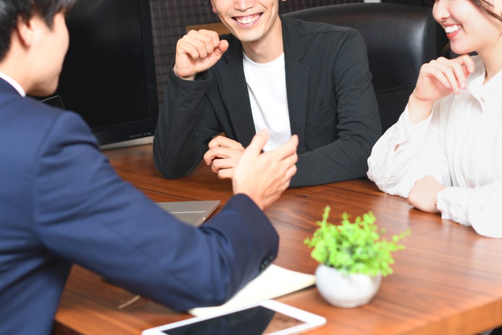 住宅相談の打ち合わせ風景。担当者と夫婦がテーブルを囲み、リラックスした雰囲気で家づくりについて会話している様子。